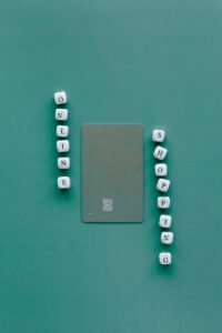 Flat lay with credit card surrounded by word "Online Shopping" on green backdrop.