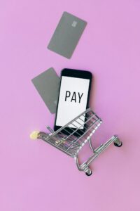 Top view of a smartphone in a shopping cart with credit cards on a purple background.